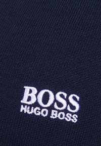 Detailní záběr na tmavě modrou pletenou látku s bílým vyšívaným logem "BOSS HUGO BOSS".