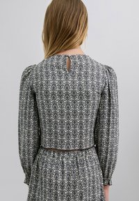 Vestido de patrón en blanco y negro con mangas largas, un escote en forma de ojo de cerradura en la espalda y una cintura ajustada con un cinturón estrecho. Tela texturizada.