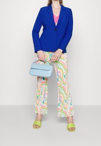 Modrá sako s jedním knoflíkem, růžový top, vzorované nabírané kalhoty v pastelových barvách a světle modrá kabelka. Zelené slip-on boty.