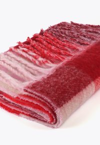 Rød og pink uld tæppe med et gradient design, der har varierende teksturer og bløde frynser, rullet og delvist udrullet.