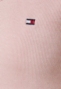 Červenobíle pruhovaná látka s texturovaným povrchem, s malým vyšívaným logem v námořnické modři, bílé a červené v levém horním rohu.