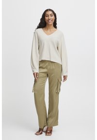 Béžový crop top s výstřihem do V a dlouhými rukávy, spárovaný s olivově zelenými cargo kalhotami s bočními kapsami a hladkou texturou.