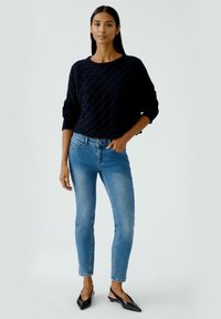 Marineblauer strukturierter Strickpullover, schmal geschnittene hellblaue Jeans und schwarze spitze Ballerinas. Das Outfit zeichnet sich durch ein entspanntes Design und einen lässigen Look aus.