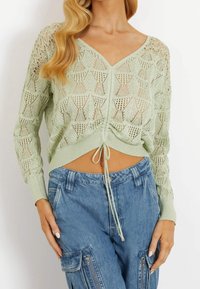Lichtgroene gebreide crop top met een V-hals, kantontwerp en treksluiting aan de zoom, in combinatie met blauwe cargobroeken met ritszakken.
