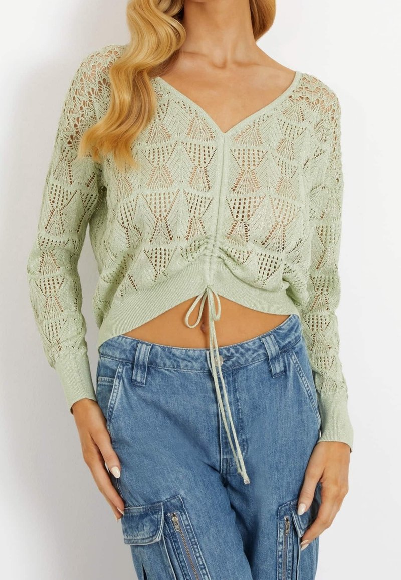 Lichtgroene gebreide crop top met een V-hals, kantontwerp en treksluiting aan de zoom, in combinatie met blauwe cargobroeken met ritszakken.
