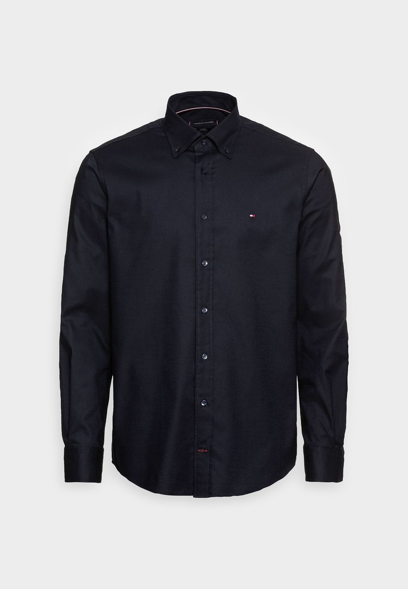 Svart långärmad skjorta i mjukt tyg, med krage som knäpps med knappar, blå knappar och en liten logotyp på vänster bröst.