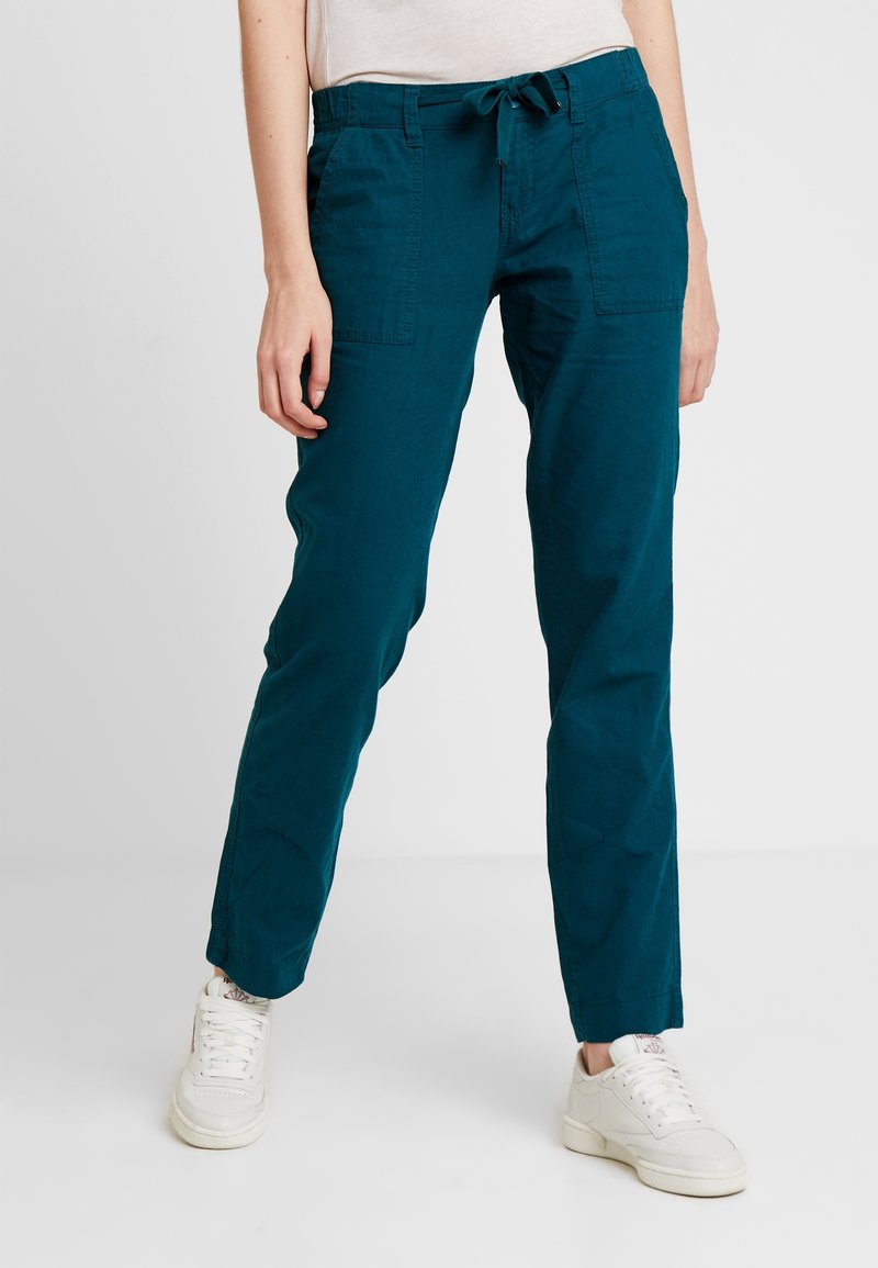 Tealfärgade byxor i bomullsblandning med dragsko i midjan, två framfickor och rak bendesign, kombinerat med vita sneakers.