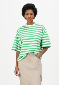 T-shirt oversize rayé vert et blanc avec un col rond et des épaules tombantes. Assorti à une jupe beige avec des poches latérales.