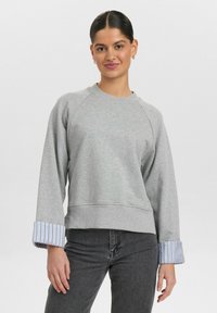 Grå sweatshirt med rund hals, raglanärmar och randigt tyg vid ärmsluten. Har en avslappnad passform och mjuk textur.