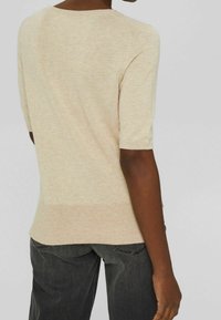 Pull à manches courtes de couleur crème avec une finition texturée, présentant un col arrondi et un ourlet côtelé, associé à un jean gris foncé.