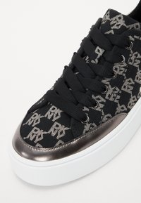 Μαύρο καμβά σας sneaker με μεταλλικό ασημί σχέδιο λογότυπο, επίπεδες μαύρες κορδόνες και μεταλλική ασημί μύτη. Έχει λευκή καουτσούκ σόλα.