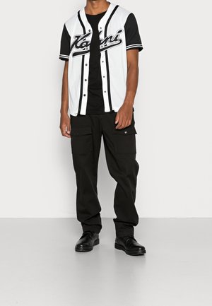 Jersey de béisbol en blanco y negro con botones, que presenta una gran impresión gráfica; combinado con pantalones cargo negros y zapatos negros.
