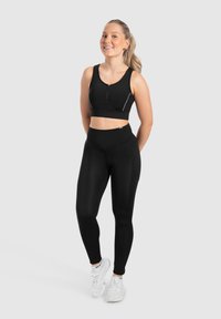 Zwarte sportieve crop top met een rits aan de voorkant en reflecterende details, gecombineerd met hoge zwarte leggings, beide gemaakt van rekbare stof.