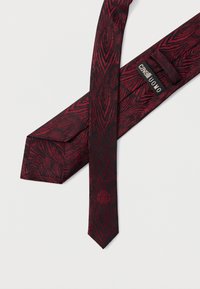 Czerwona i czarna krawat z wzorem przypominającym fakturę drewna. Posiada zwężający się koniec oraz metkę z napisem "Cavalli Uomo".