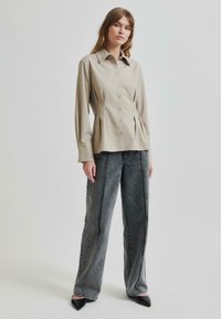Beige langermet skjorte med knapper og tilpasset midje og legg, kombinert med høyt midje grå vide jeans med kontrasterende sømmer.