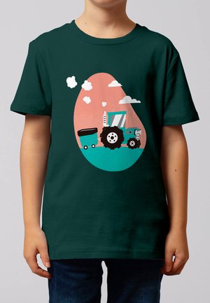 Kind trägt dunkelgrünes Hemd mit einem türkisfarbenen Traktor, der einen Anhänger vor einem rosa und türkisfarbenen ovalen Hintergrund mit weißen Wolken zieht.