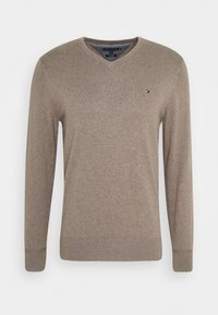 Beige V-Ausschnitt-Pullover aus weichem Strickstoff. Mit langen Ärmeln und gerippten Bündchen. Kleines Logo-Element in der Nähe des Ausschnitts.