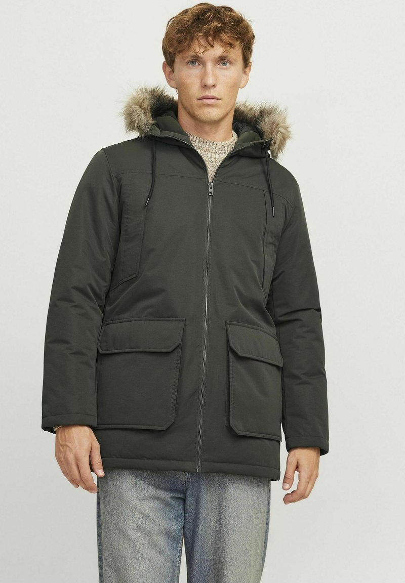 Donkergroene parka met een ritssluiting, twee voorkruiszakken en een met bont gevoerde capuchon. De stof lijkt glad met een matte afwerking en een robuust ontwerp.