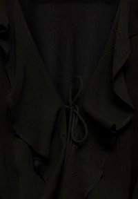 Tissu noir avec un col à volants et un nœud en corde attaché au centre, suggérant le devant supérieur d’un chemisier ou d’une robe.