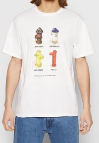 Vit bomull t-shirt med illustrationer av fyra färgglada brandposter märkta med stad: New York, San Francisco, Los Angeles och Tokyo.