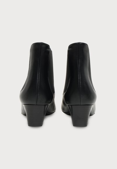 Paire de bottines en cuir noir à talons blocs, vues de dos sur un fond clair uni.