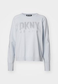 Ljusblå sweatshirt med ribbade muddar, rundad halsringning och "DKNY JEANS" tryckt i silverglitter över framsidan. Mjuk material och avslappnad passform.