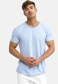 Lyseblå t-shirt med korte ærmer og rund halsudskæring, tekstureret stof og buet kant, båret over lyse bukser.