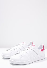 Vita lädersneakers med rosa hälaccent, perforerade detaljer på sidorna och platta snören. Gummisula och logotyp på hälen.