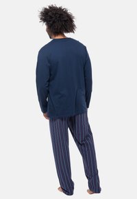 Maglione a maniche lunghe blu navy abbinato a pantaloni da pigiama a righe con linee viola, rosse e bianche. I pantaloni hanno un elastico in vita e una vestibilità comoda.