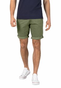 Grüne Baumwollshorts mit umgeschlagenen Säumen, kombiniert mit weißen Sneakers. Die Shorts haben einen geraden Schnitt und eine Fronttasche.