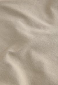 Beige stof med en glat overflade, der viser bløde folder og en subtil glans. Materialet ser ud til at være bomuld eller en bomuldsblanding.