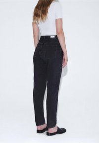 Högmidjade svarta denimjeans med rak passform och synlig sömnad. Bakfickor och en märkesetikett på midjan. Slät textur.