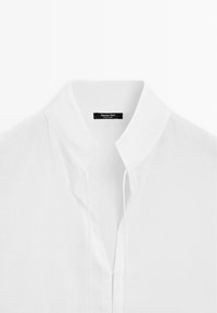 Hvid skjorte med krave, forrest med knapper og et mærke med teksten "Massimo Dutti" ved halsudskæringen.