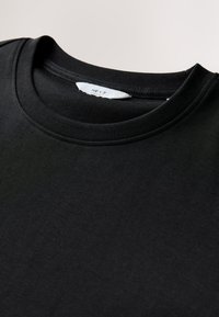 Black cotton t-shirt with a crew neckline, flat seams, and a label inside the collar. Smooth texture, casual design, no patterns or embellishments.