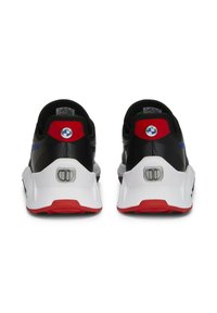 Baskets noires avec une semelle blanche, accents rouges et une bande bleue. Présente un logo circulaire au niveau du talon et une surface texturée.