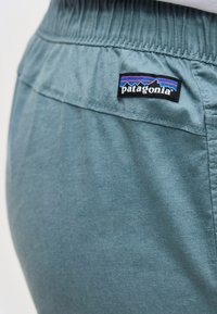 Κοντινό πλάνο παντελονιού με ελαστική μέση σε τιρκουάζ χρώμα με λογότυπο Patagonia που περιέχει σχεδιασμό βουνού και ρίγες σε μπλε, μωβ και μαύρο.