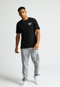 Must musta T-särk valgete tähtedega, koos heledate hallide cargo-pükstega, millel on lukuga taskud ja reguleeritavad mansetid, ning valged spordijalatsid.