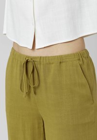 Pantalons en mélange de coton léger couleur vert olive avec une taille élastique et un cordon de serrage, présentant une texture lisse et des poches latérales.
