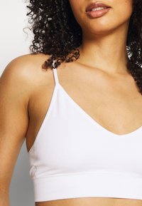 Bralette bianco a coste con scollatura a V profonda, spalline sottili e tessuto testurizzato. Presenta un design aderente per il massimo comfort.