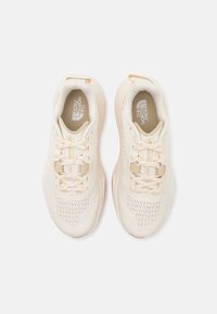 Beige sportieve schoenen met een gebreide bovenkant, ronde neus, gevoerde kraag en platte veters, met logo-detail op de tong.