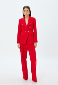 Rode dubbelzijdige blazer en bijpassende broek gemaakt van textuurstof. De blazer heeft gouden knopen en scherpe revers.