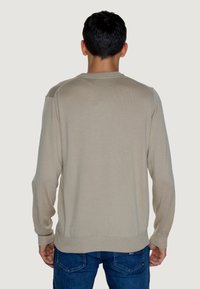 Maglione beige in maglia con maniche lunghe, scollo rotondo, polsini e orlo a costine. Design semplice, texture morbida, forma aderente e dettagli minimali.