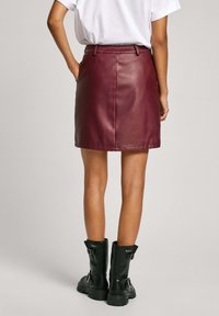 Burgundská mini sukňa z imitácie kože s priliehavým strihom, pútkami na opasok a hladkým povrchom. Nosená s čiernymi členkovými boots s prackami.