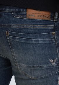 Temno modri jeans iz denima z usnjenim oznako "PME Legend" in izvezenim logotipom s krili na zadnjem žepu.