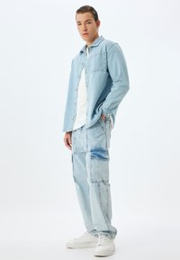  Lichtblauwe denim shirt met een voork Pocket, gecombineerd met bijpassende cargo-stijl jeans met patchaccenten. Witte sneakers maken de look compleet.