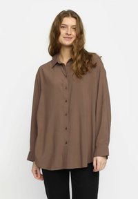 Chemise brun à col, coupe décontractée, manches longues et texture lisse. Présente un ourlet droit et des détails de boutons.