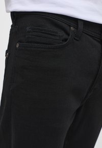 Jeans de mezclilla negra con un ajuste clásico, diseño de cinco bolsillos y detalles de costura sutiles. La tela parece duradera con una textura suave.