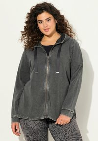 Sudadera con cremallera de color gris, con una textura suave, capucha con cordón y mangas largas. Combinada con leggings estampados que presentan motivos de animales.