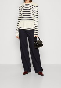 Pull à peplum rayé en crème et marine, associé à un pantalon large en denim foncé. Accessoirisé avec un petit sac à main noir et des chaussures à bout pointu.