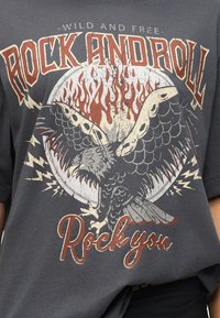 Σκούρο γκρι πουκάμισο με γραφικό αετού σε vintage στυλ, φλόγες, κεραυνούς και το κείμενο «Άγρια και ελεύθερα Rock and Roll Rock you.»